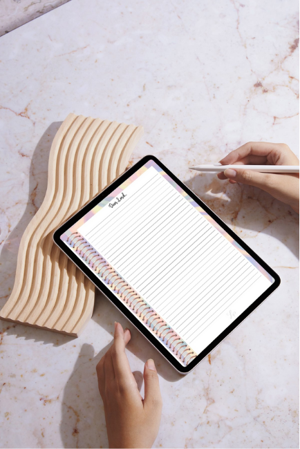  A tablet displays a colorful digital journal page titled "Brain Dump," set on a marble surface. A hand with a stylus is ready to write, alongside a stylish wooden accessory, highlighting creativity and productivity.